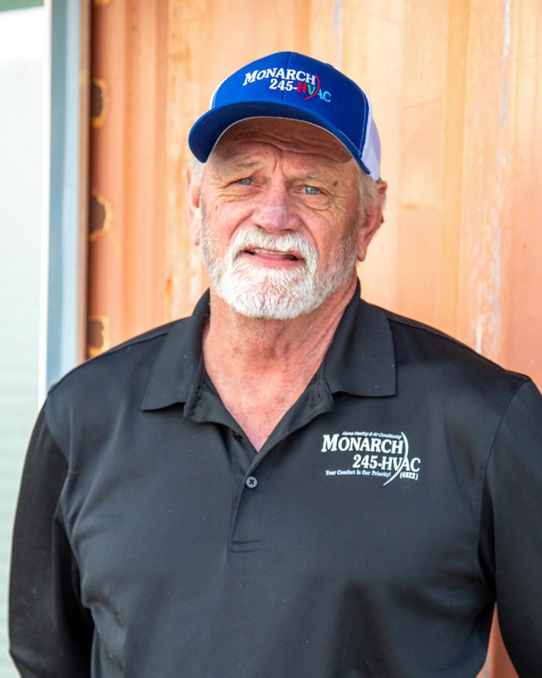 Man wearing a blue Monarch 245-HVAC hat and shirt, standing outside with a neutral expression.