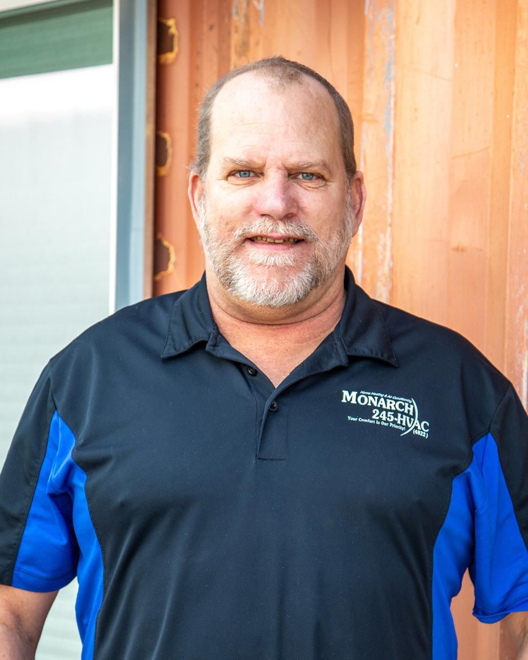 Man in black and blue polo shirt, smiling, standing outside a building.