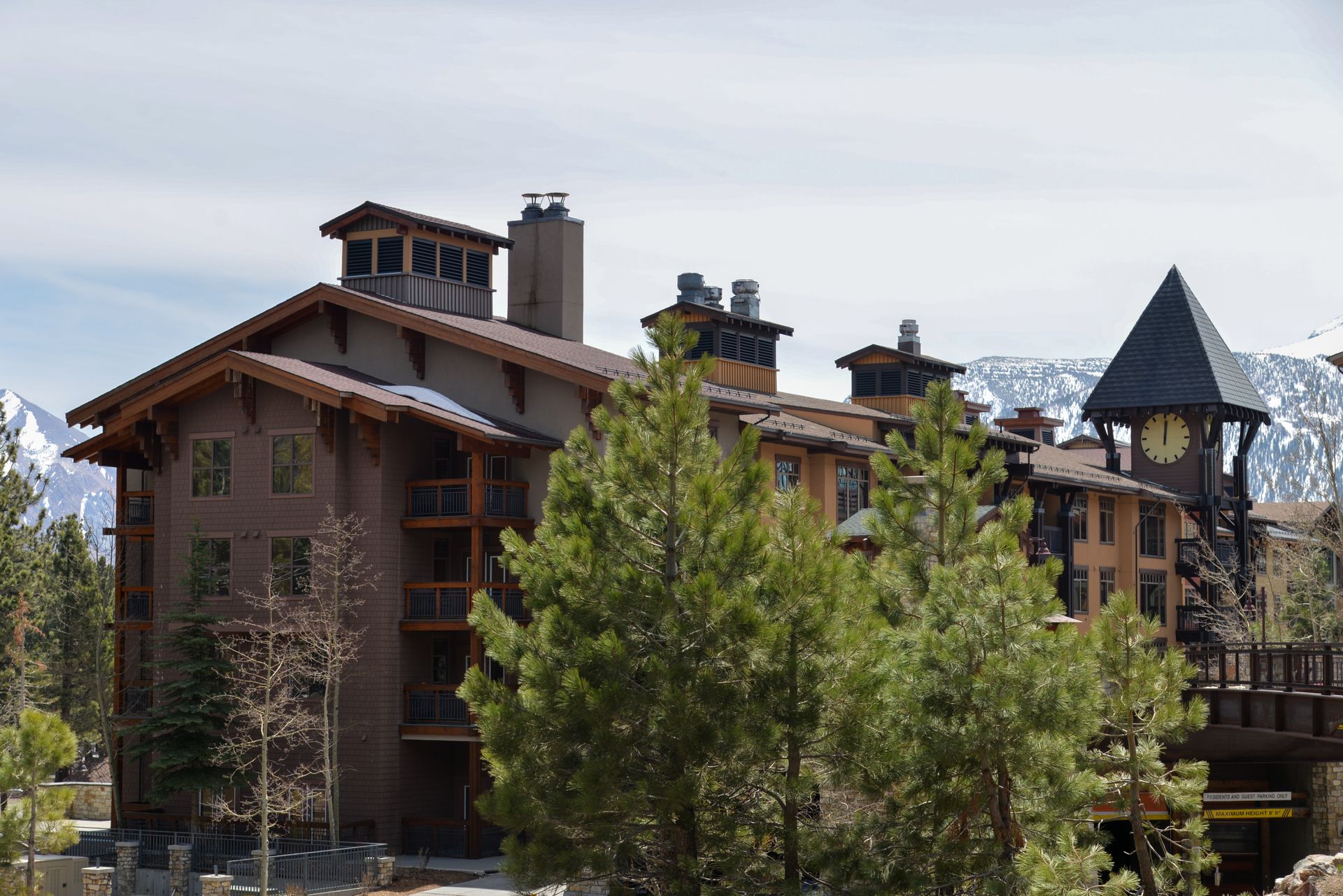 Rustic mountain lodge with brown roofs and a tower, surrounded by trees under a clear sky