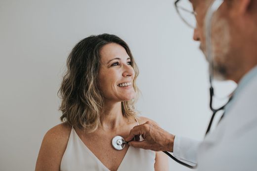 Doctor checking a smiling patient's heartbeat with a stethoscope in a bright exam room