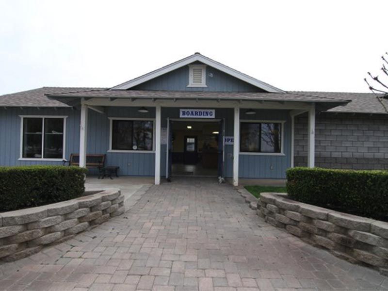 Front entrance of a small blue-gray building with a brick walkway and stone retaining walls