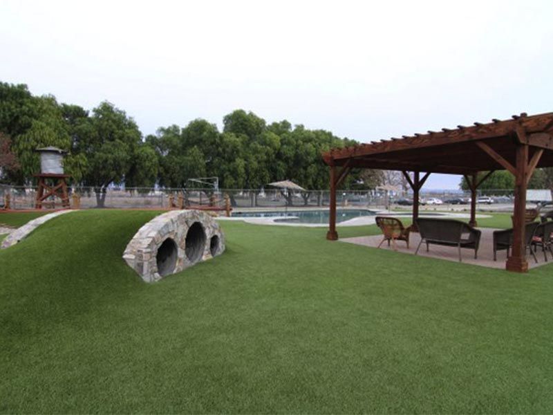 Grassy park with a stone tunnel, wooden gazebo, picnic table, and trees by a fenced pond