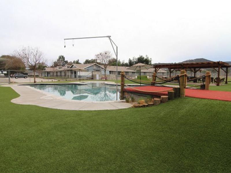 Pool with diving board, red walkway, and green lawn at an outdoor recreation area