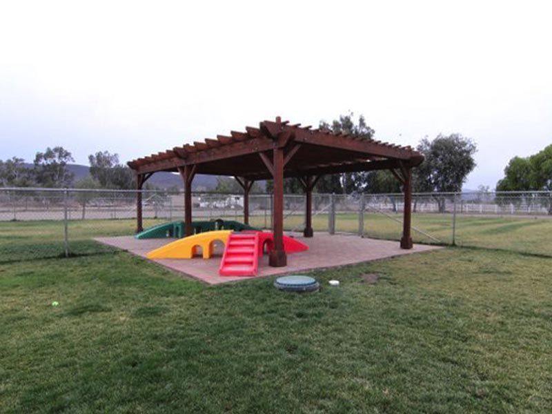Wooden pergola over a colorful play structure in a grassy park field