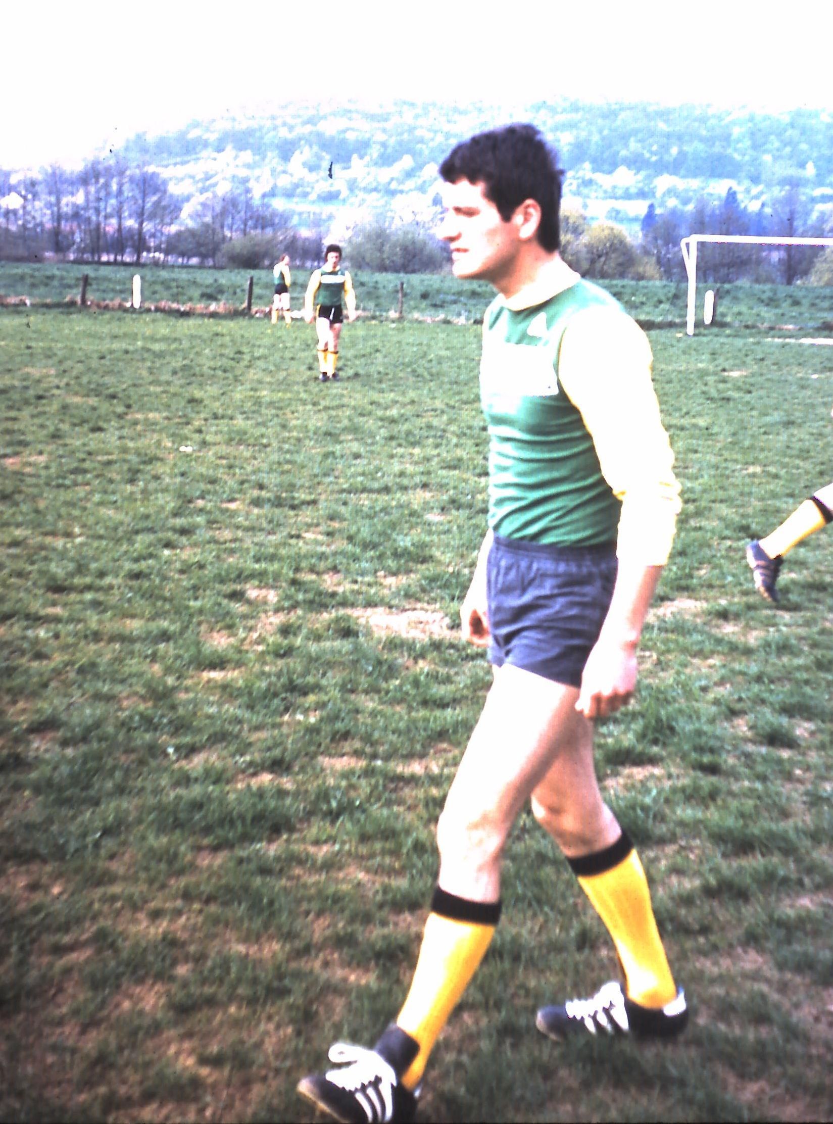 Un homme en chemise verte et short bleu marche dans un champ