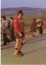 Un homme en chemise rouge et en short marche dans une rue.