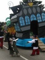 Un groupe de personnes en costumes de pirates marchent dans une rue devant un grand bateau pirate.