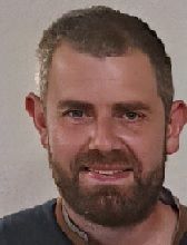 Un homme avec une barbe sourit à la caméra.