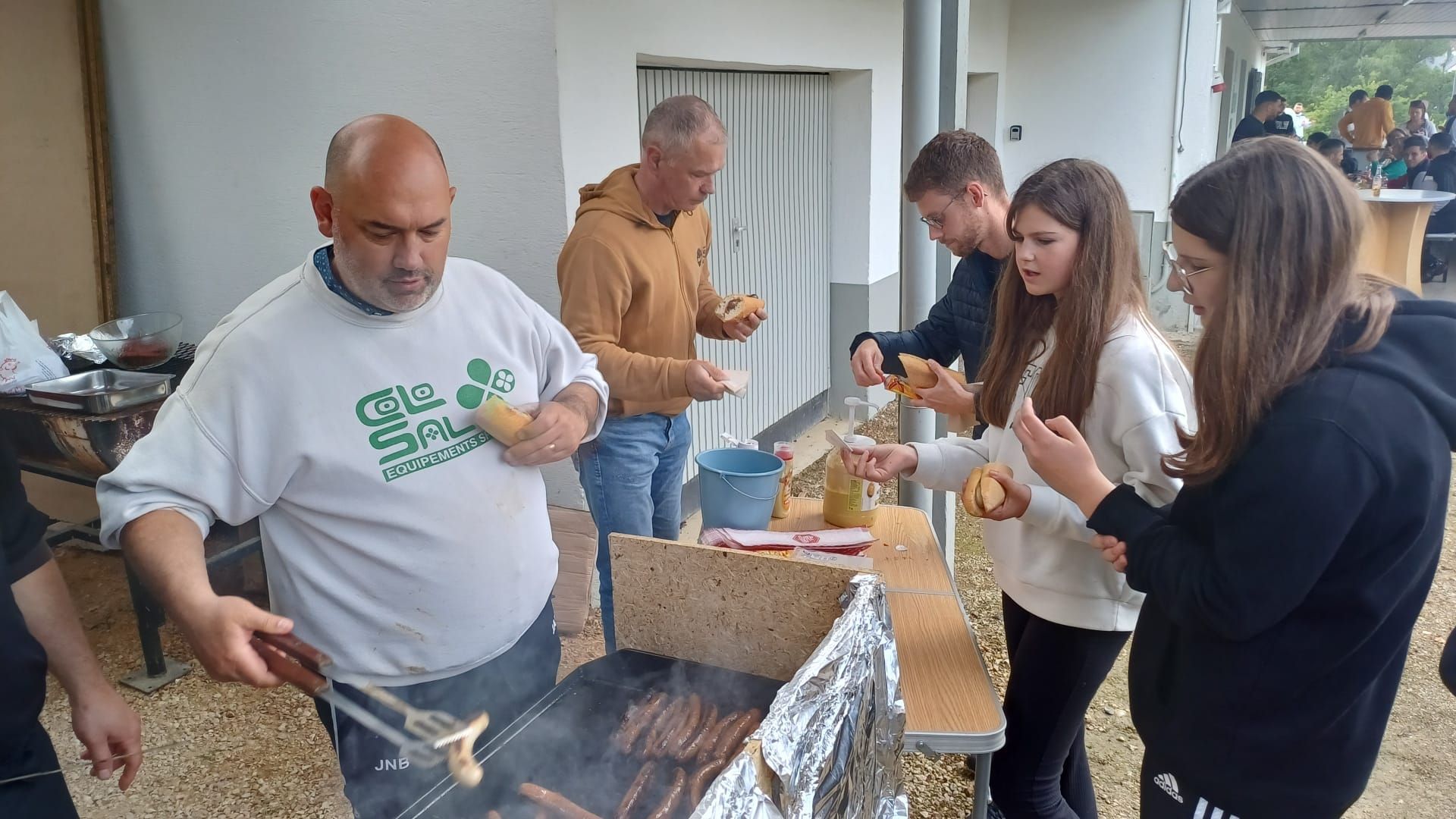 Un groupe de personnes se tient debout autour d'un gril et mange de la nourriture.