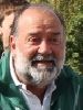 Un homme avec une barbe porte une veste verte et sourit.