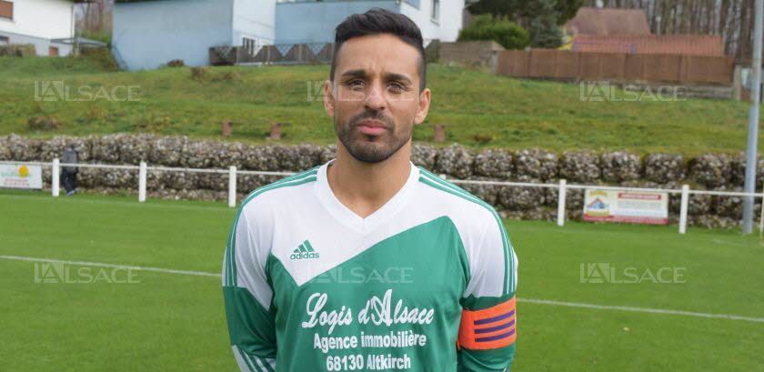 Un homme se tient debout sur un terrain de football portant un maillot vert et blanc.