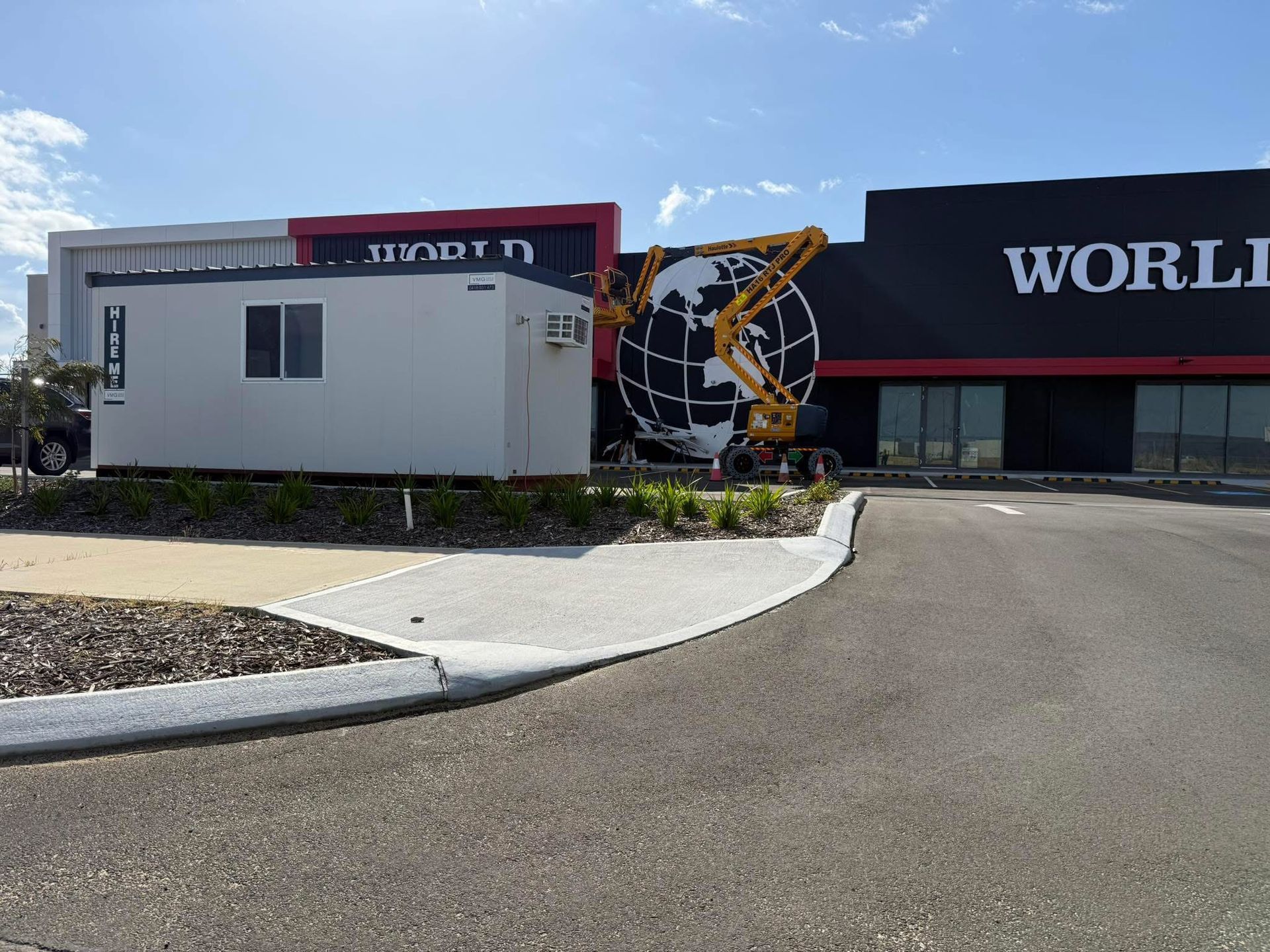 Parking lot outside a storefront with a large “WORLD” sign and a globe sculpture near the entrance.