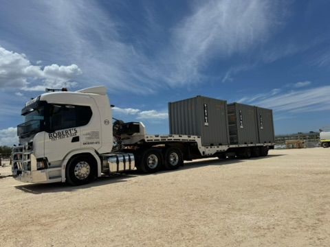 White semi-truck hauling two gray cargo containers on a gravel lot under a blue sky