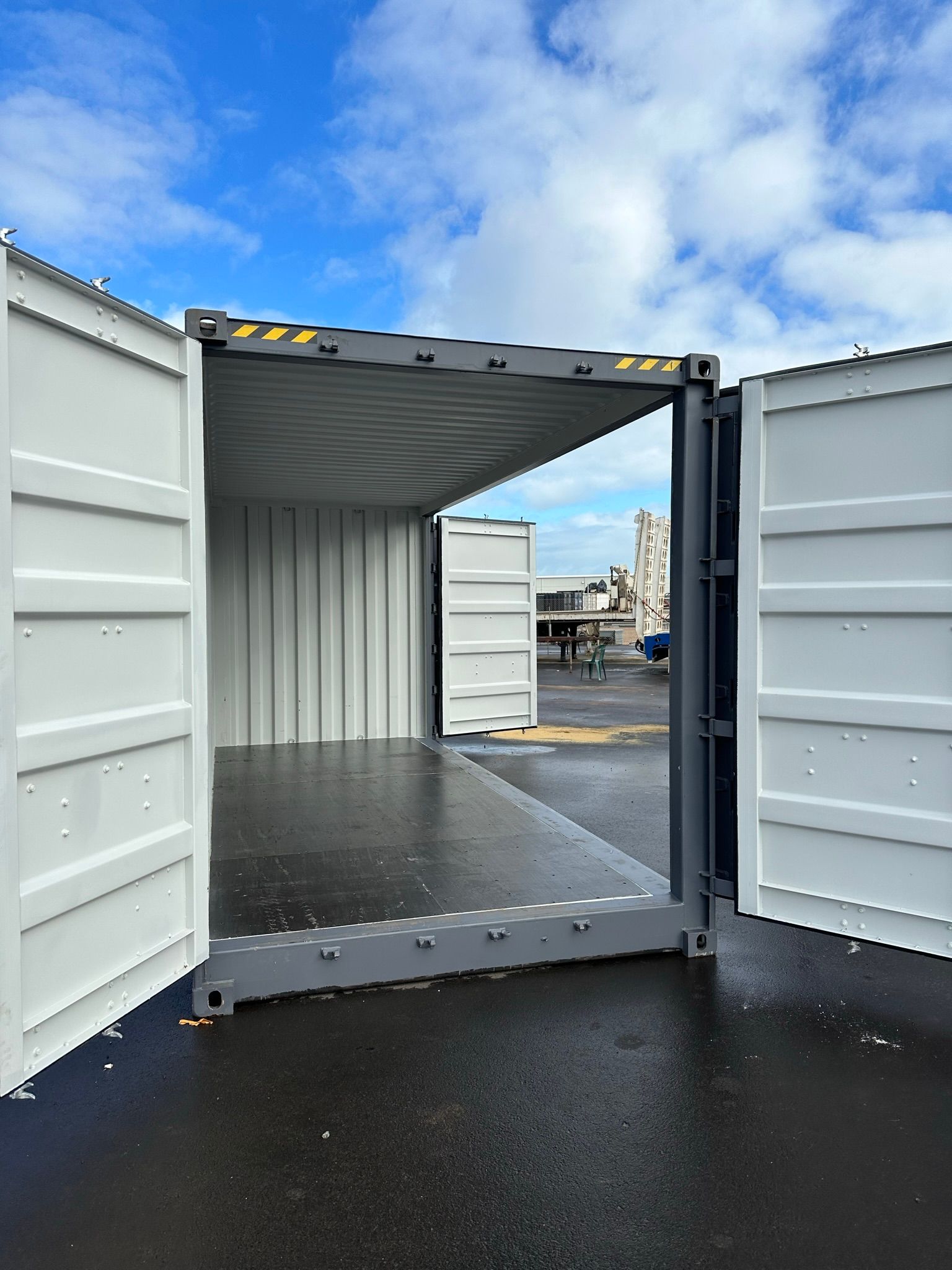 Open shipping container with doors wide open on a wet lot under a cloudy sky