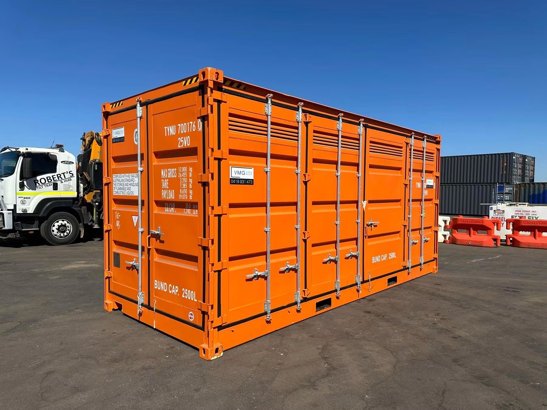 Orange shipping container on a truck yard under a clear blue sky