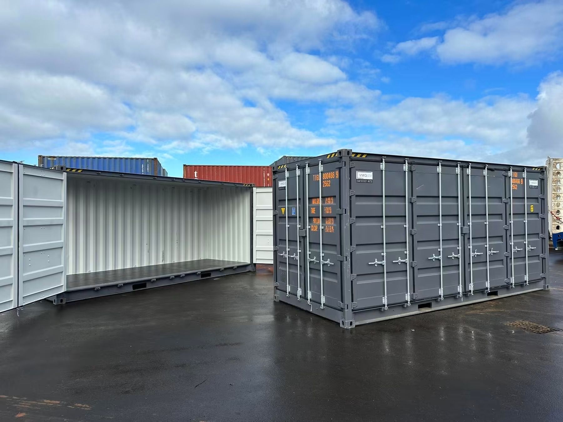 Two shipping containers on wet asphalt under a cloudy blue sky
