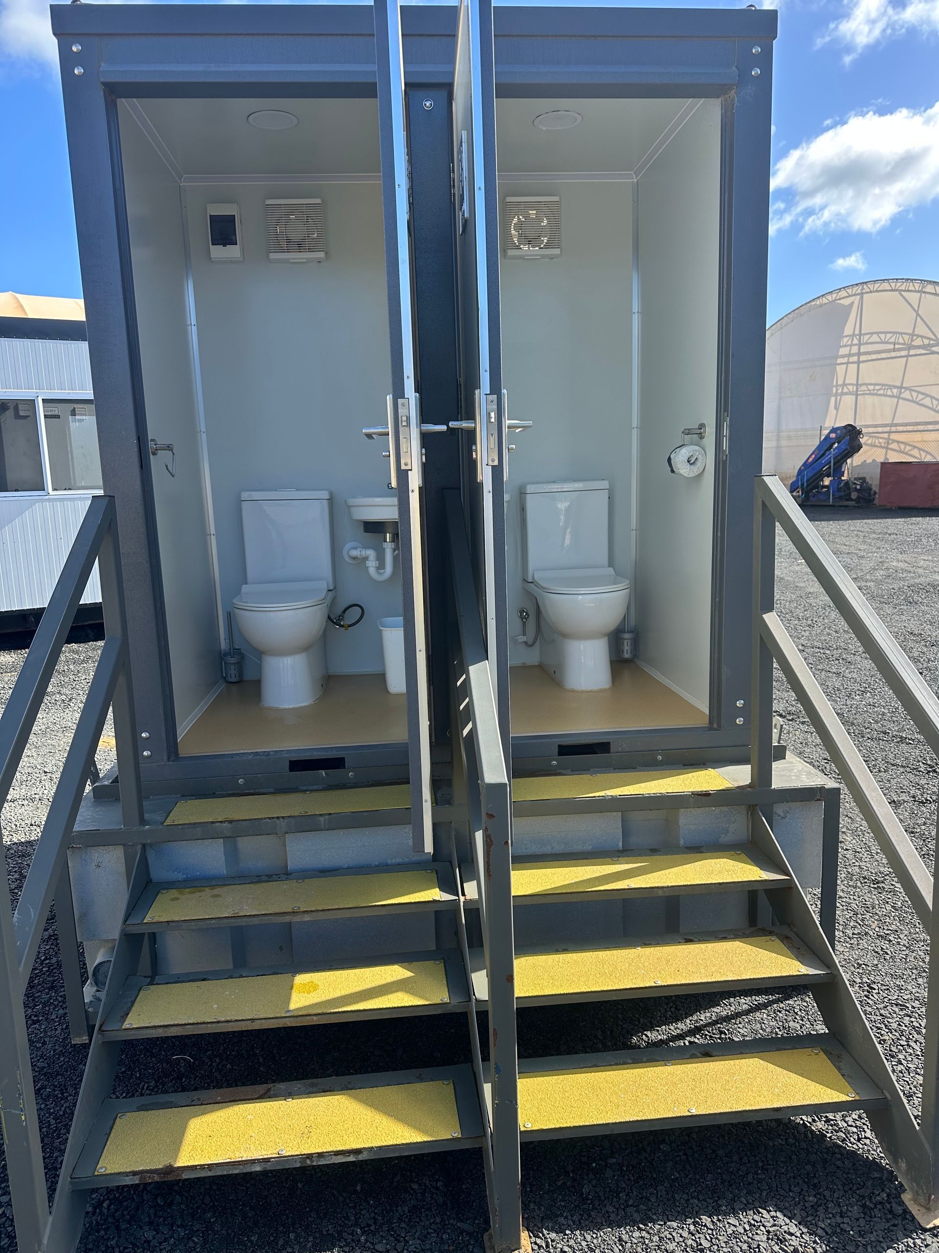 Two portable toilets at a construction site, with metal stairs and yellow step markings.