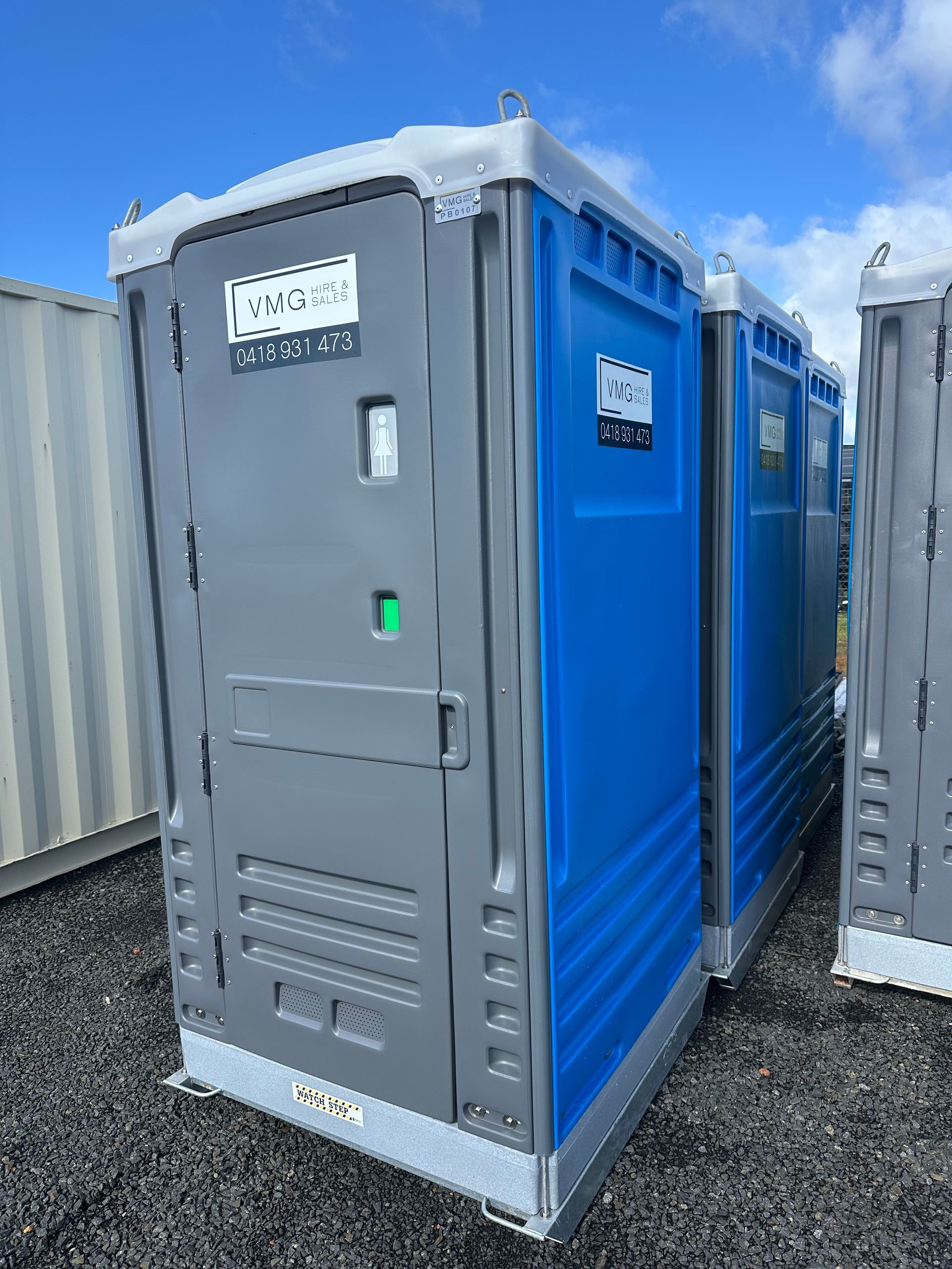 Blue portable toilet unit on gravel outdoors under a cloudy sky