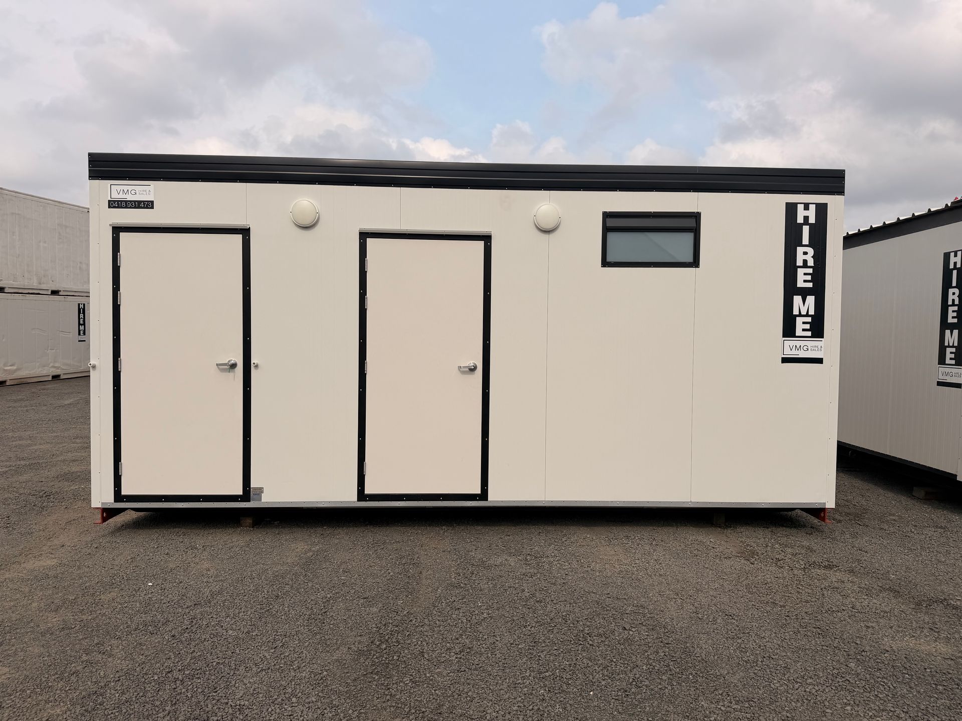 Portable beige modular office unit with two doors and a small window on a gravel lot