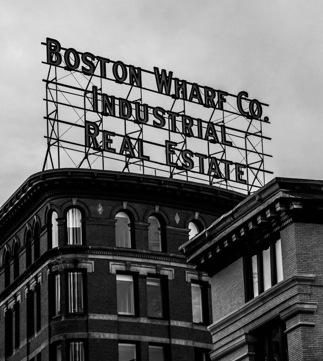 Black-and-white rooftop sign reading “Boston Wharf Co. Industrial Real Estate” on a brick building