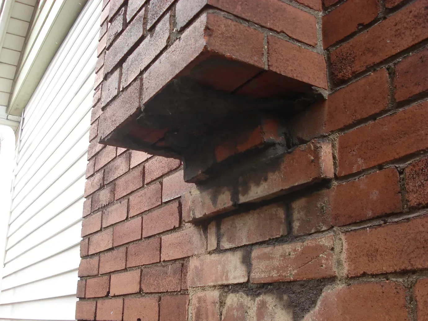 A low-angle view of a brick chimney showing a protruding section with visible mortar deterioration and soot stains.