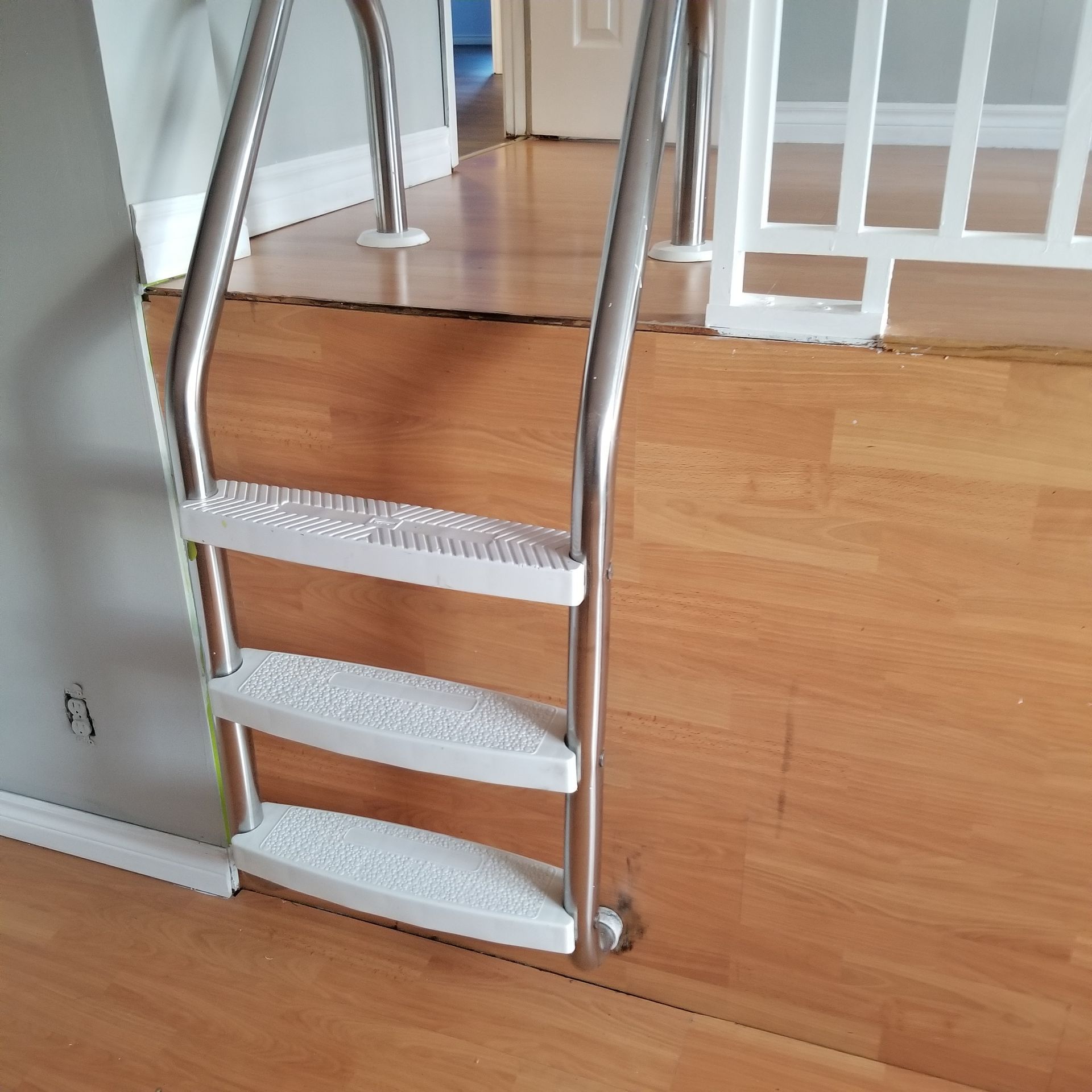 A stainless steel pool-style ladder mounted to a raised wooden platform in a room.