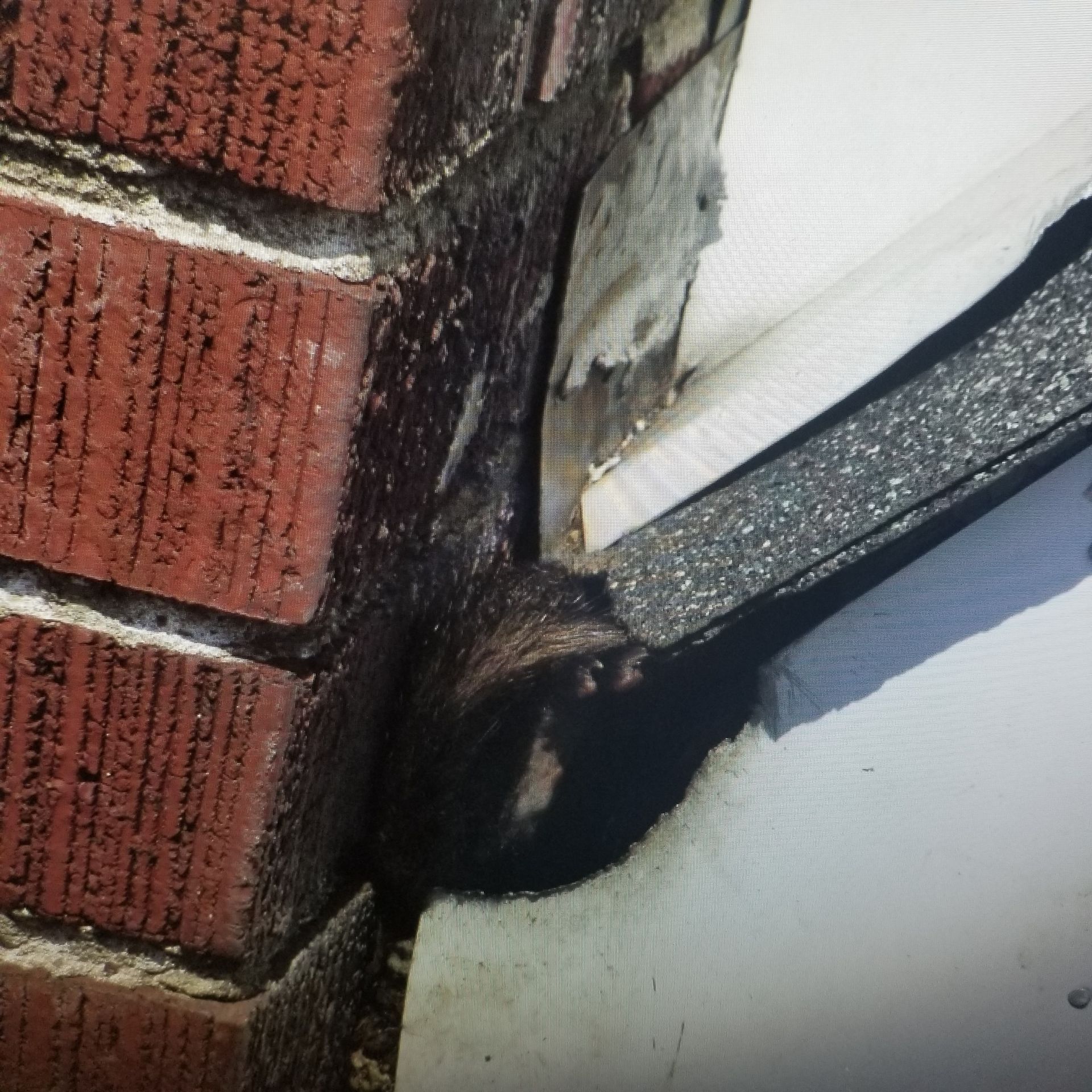 A close-up view of a brick chimney meeting a roof, showing damaged flashing and a large black glob of excess sealant.