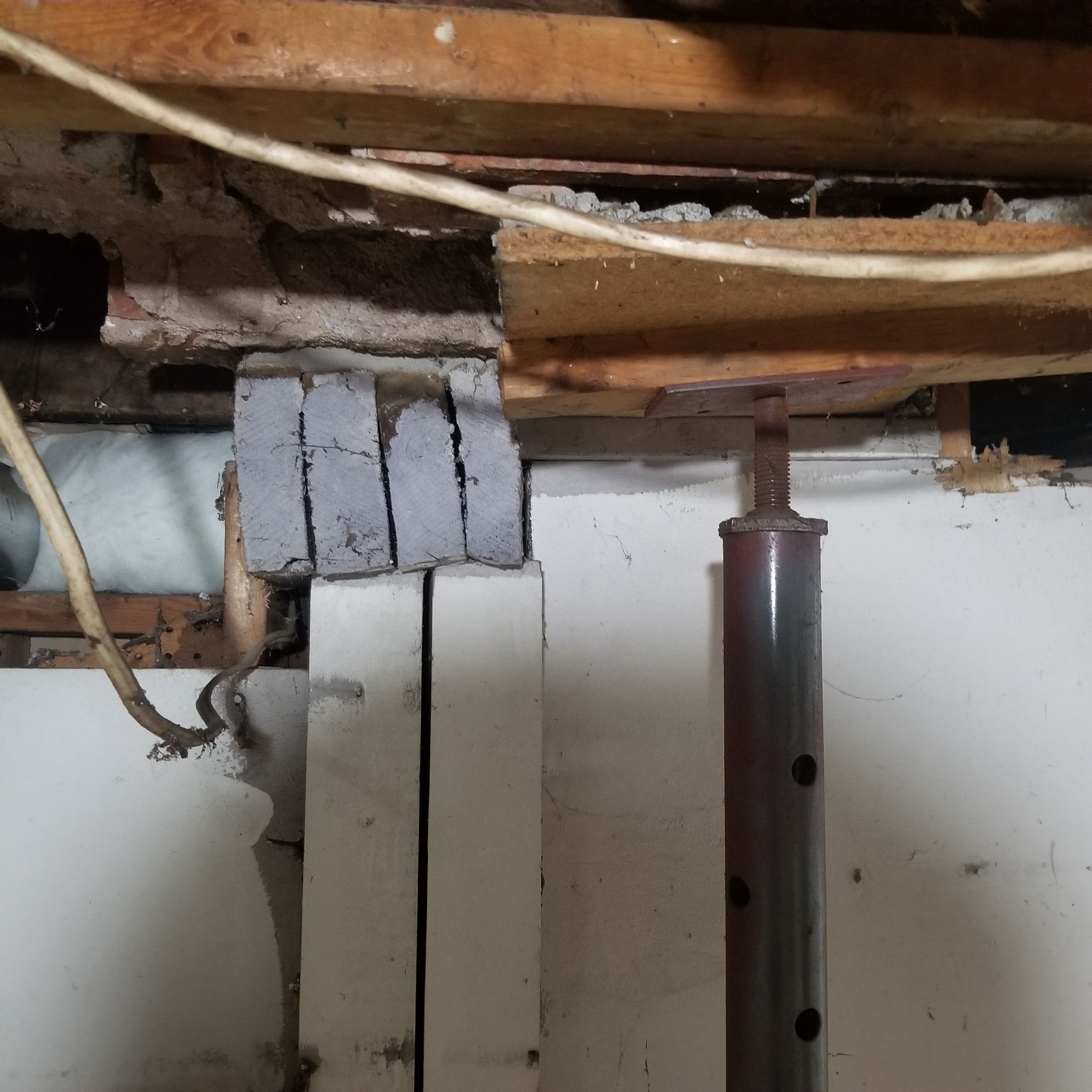 A basement support structure featuring concrete blocks stacked on wooden posts, next to a metal screw jack.