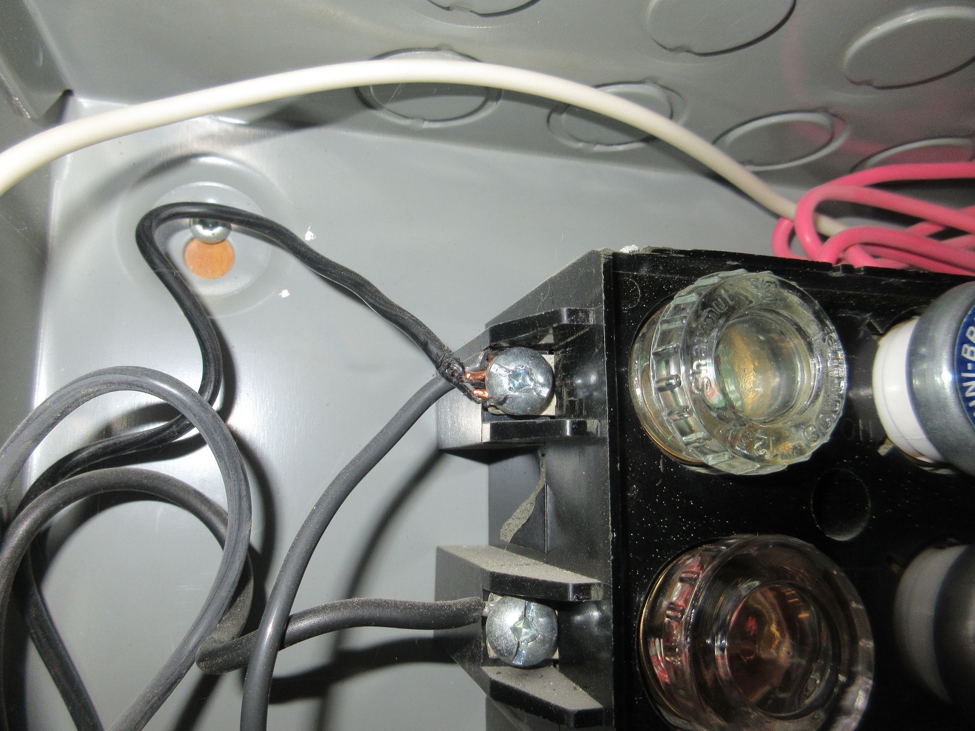 A close-up view of two black electrical wires connected to metal terminals on a fuse block inside a metal junction box.