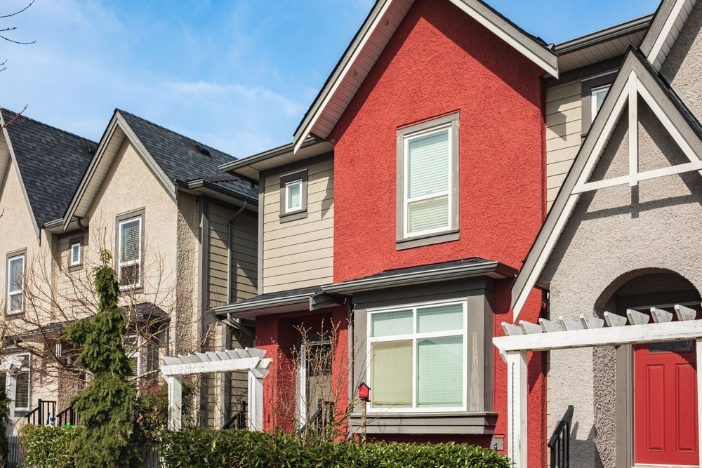 A row of modern townhouses featuring textured siding in beige and red, with peaked roofs and matching front doors.