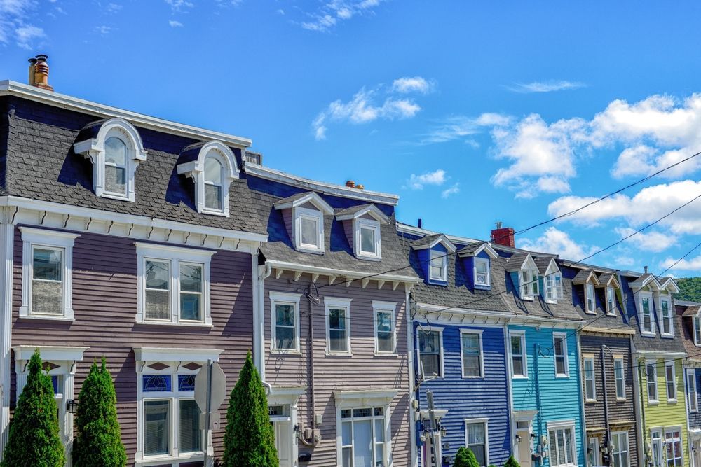A row of colorful houses with mansard roofs under a bright blue sky with scattered clouds.
