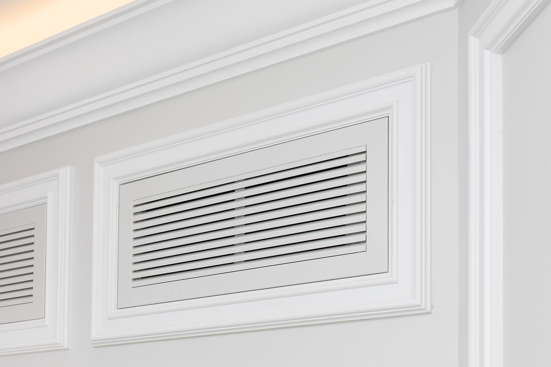 Bocchetta di ventilazione HVAC a lamelle bianche, montata su una parete chiara e pulita con finiture decorative.