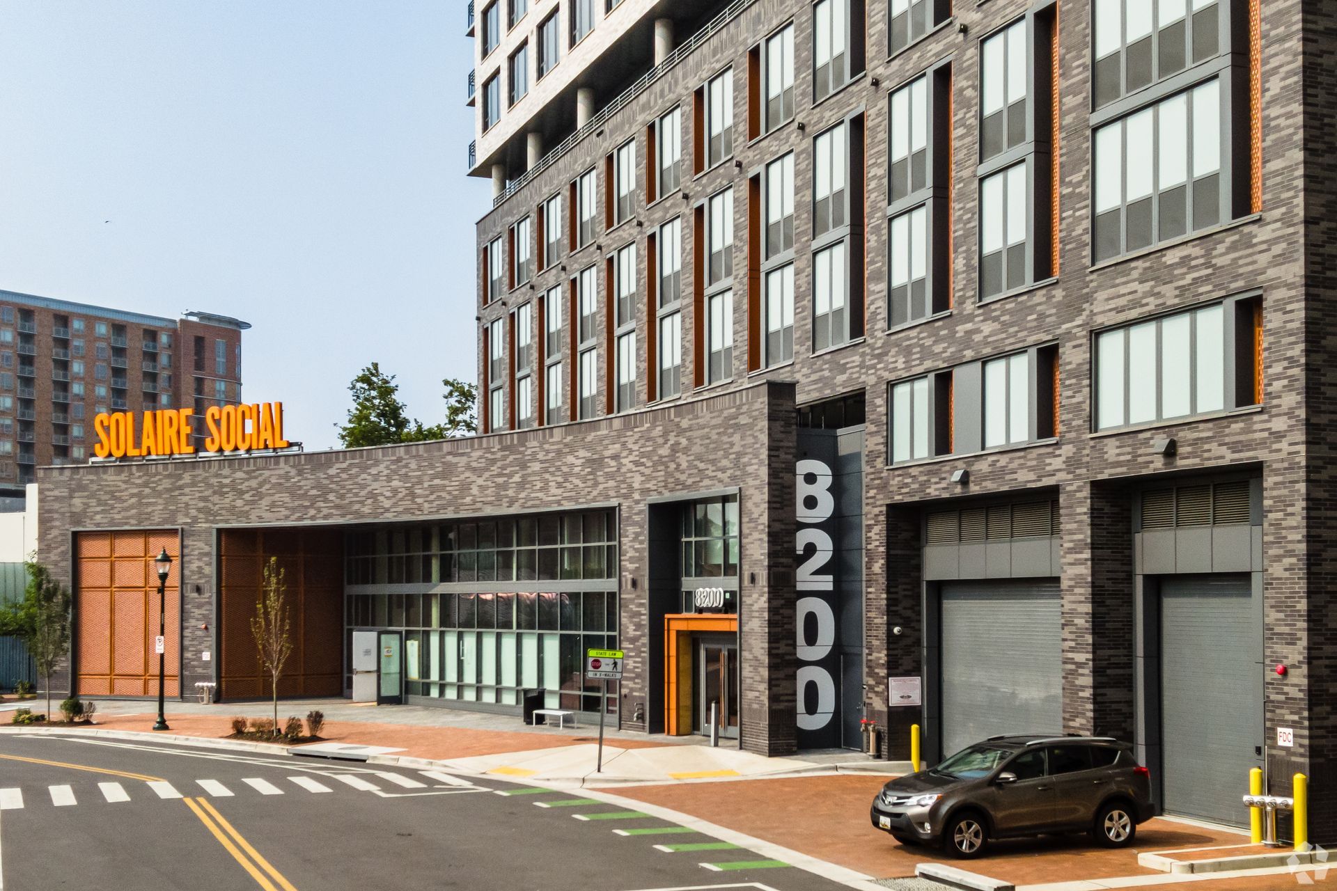 A car is parked in front of a large brick building at Solaire 8200 Dixon offers pet-freindly apartments in Silver Spring, MD.