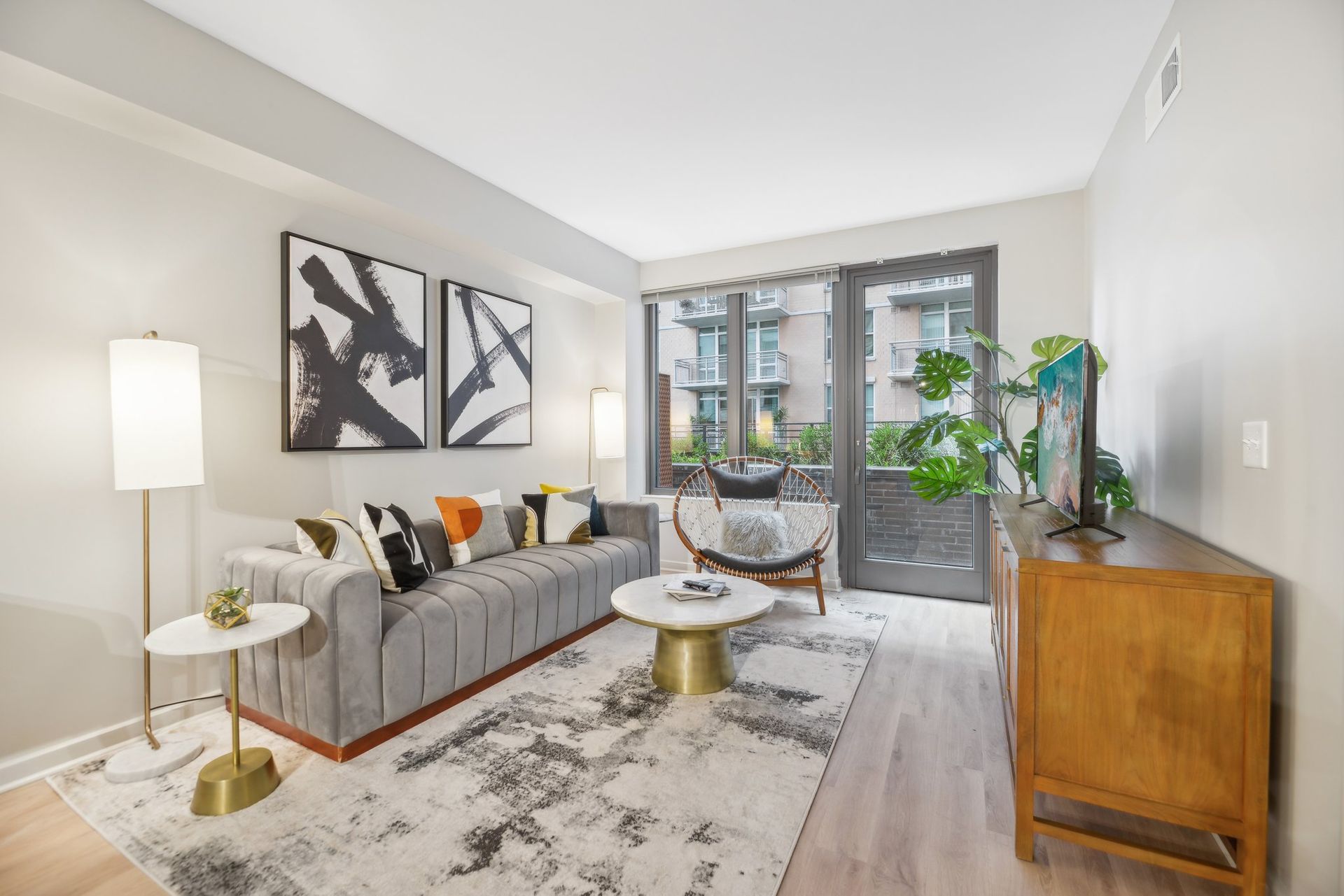 A living room with a couch, chair, coffee table, balcony, and dresser at Solaire 8200 Dixon offers apartments in Silver Spring, MD.