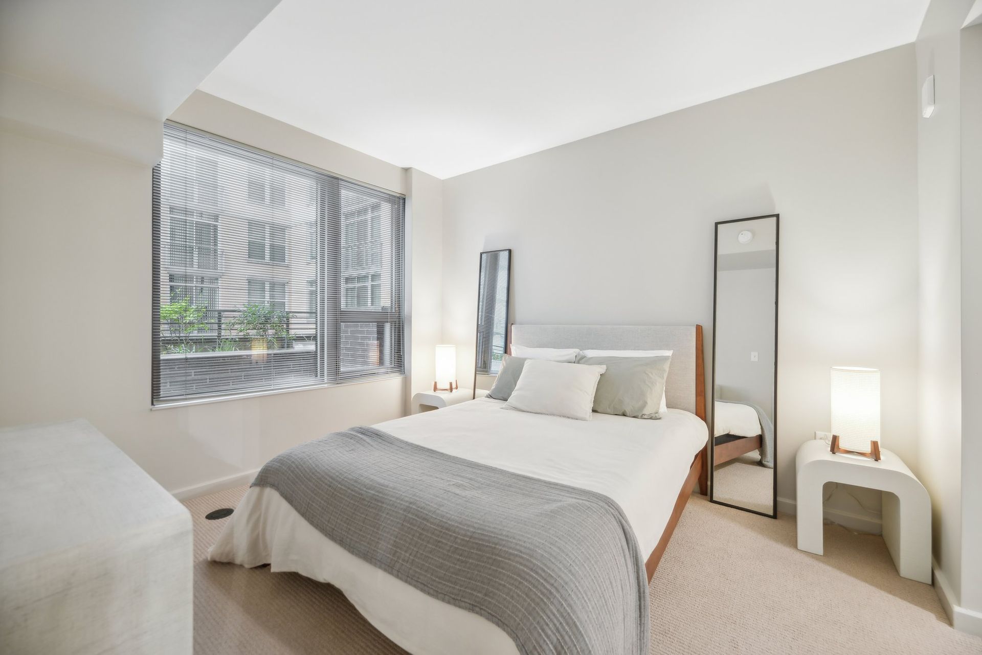 A bedroom with a bed, mirror, nightstand, and window at Solaire 8200 Dixon offers apartments in Silver Spring, MD.