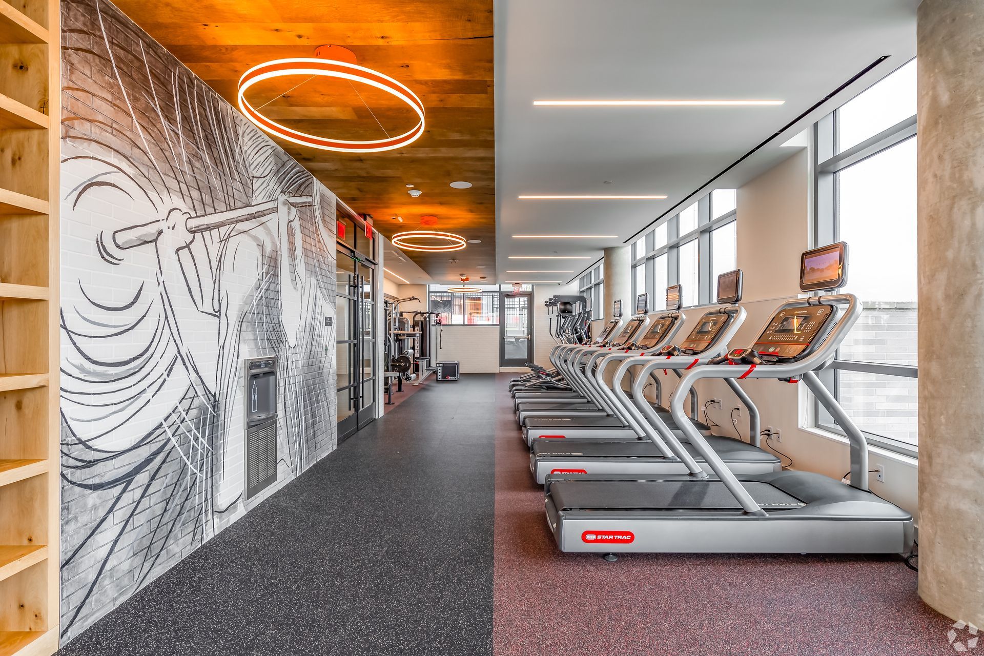 A gym with a lot of treadmills and a mural on the wall.