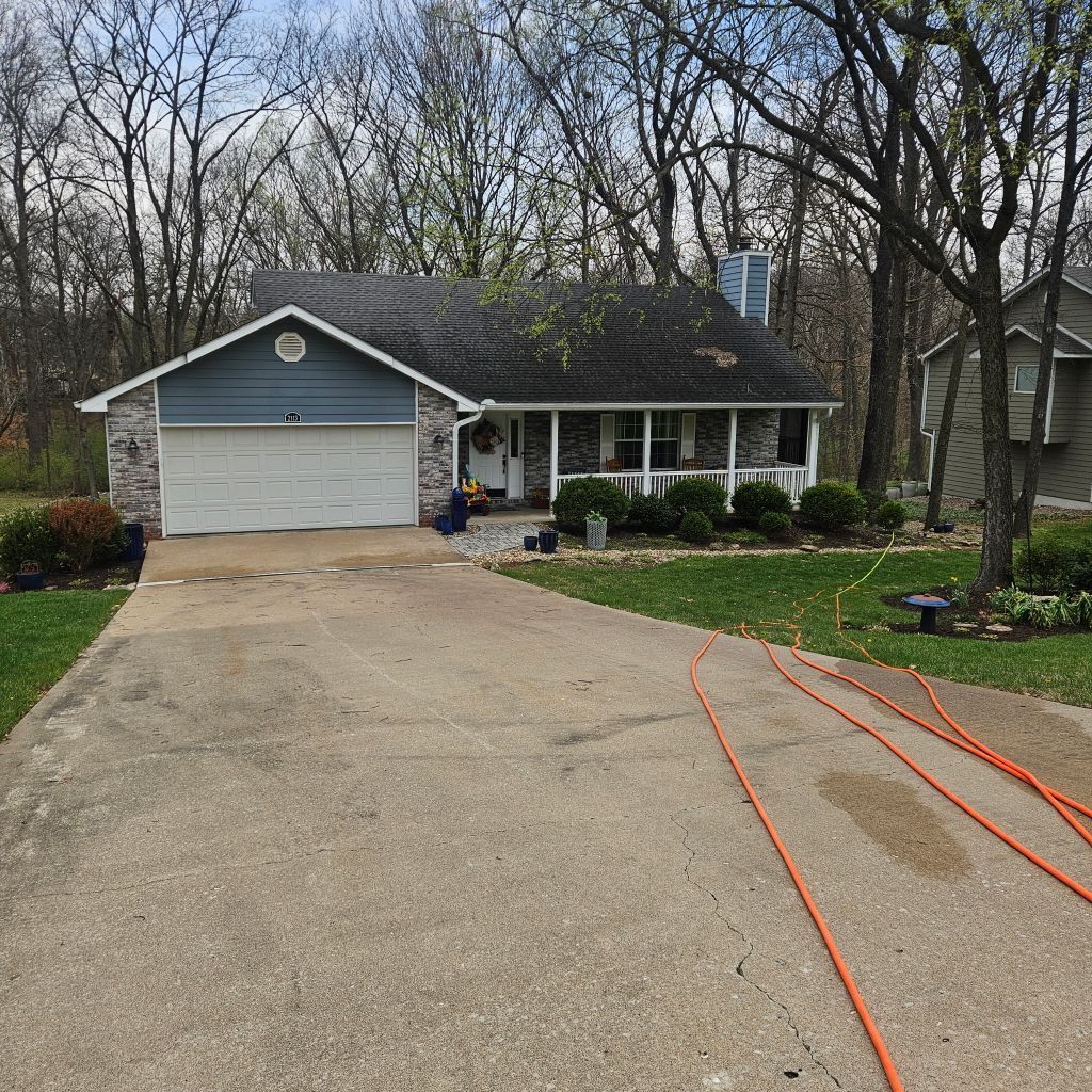 Suburban house with gray siding, attached garage, and a wide driveway in a wooded yard