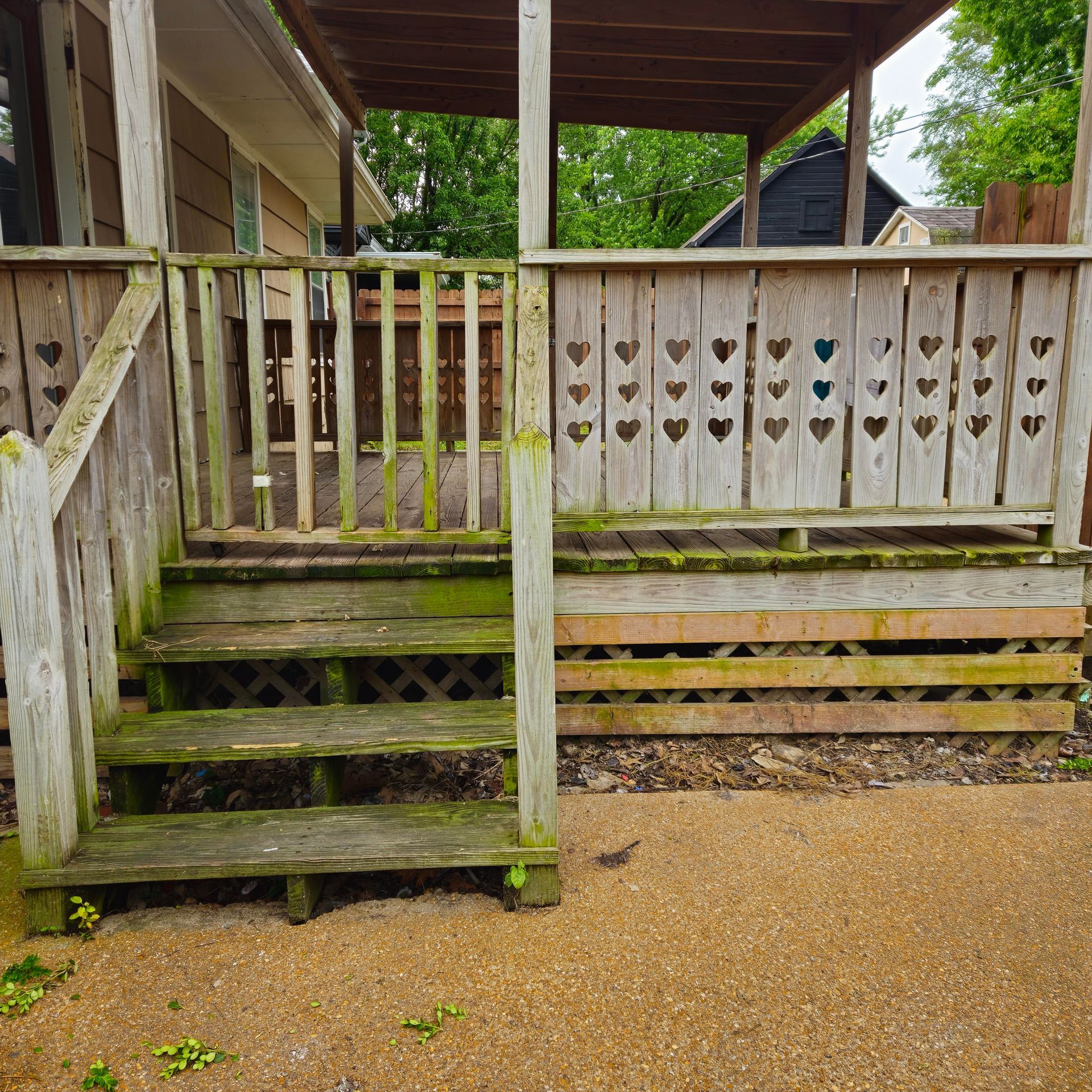Weathered wooden porch stairs and deck with heart-cutout railing beside a gravel yard