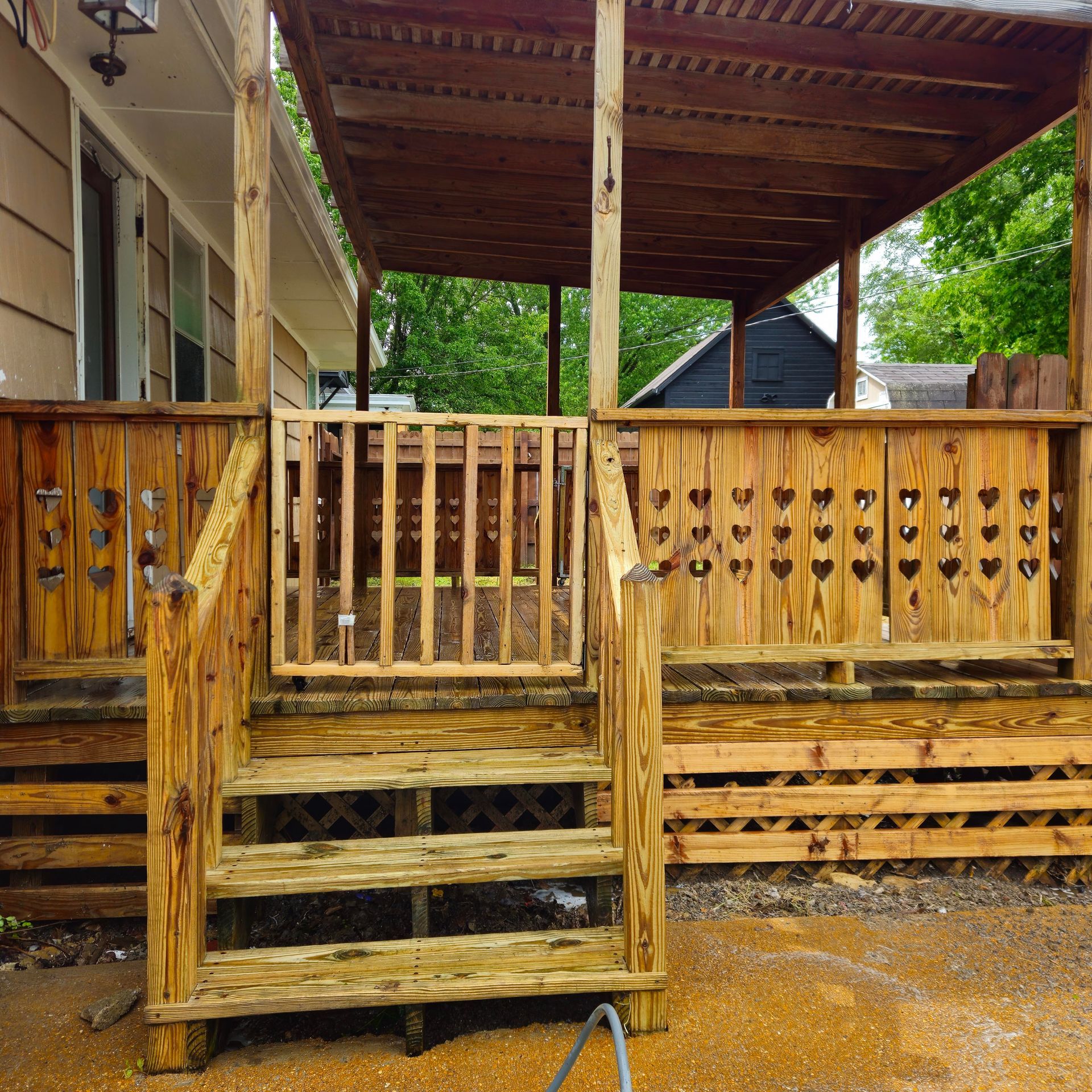 Weathered wooden porch with railings and steps under a roof, beside a house in a muddy yard