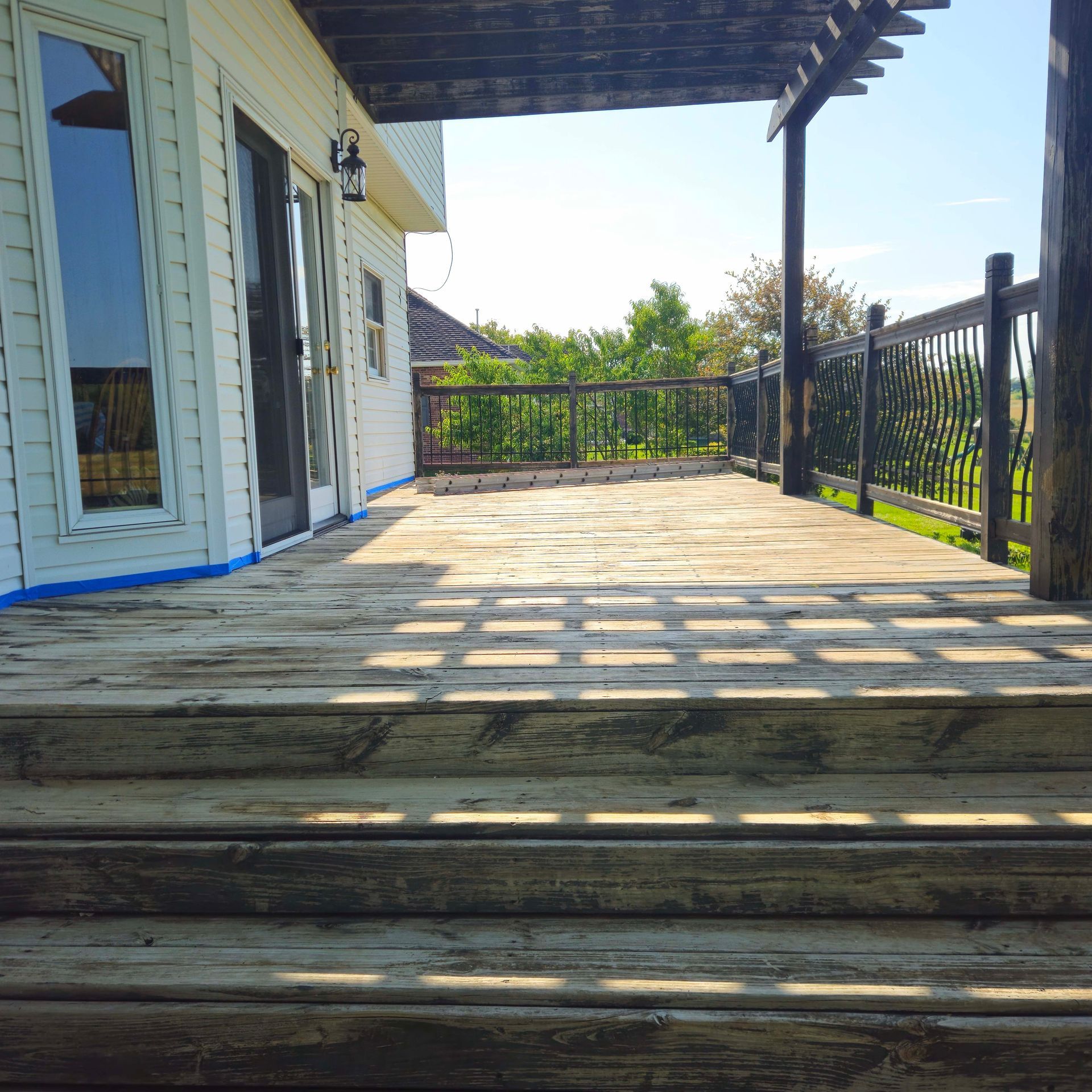Wooden porch deck with railings and steps beside a white house on a sunny day