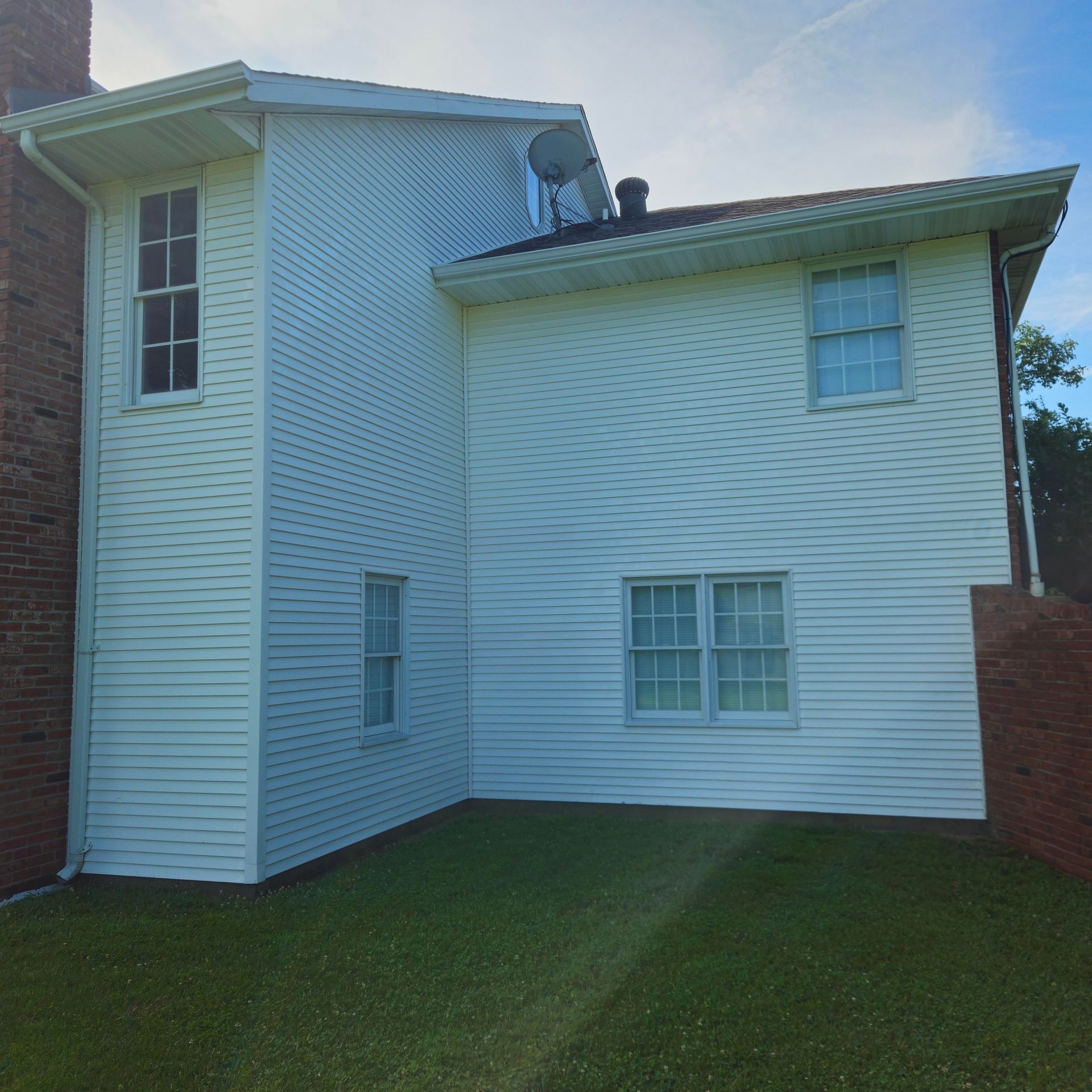 White two-story house with a small lawn, brick sides, and multiple windows under a sloped roof.