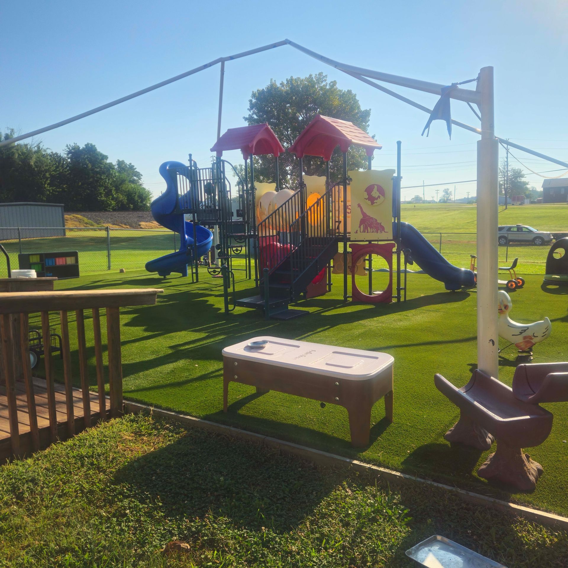 Children’s playground with blue slide, red-roof play structure, benches, and grassy park area on a sunny day