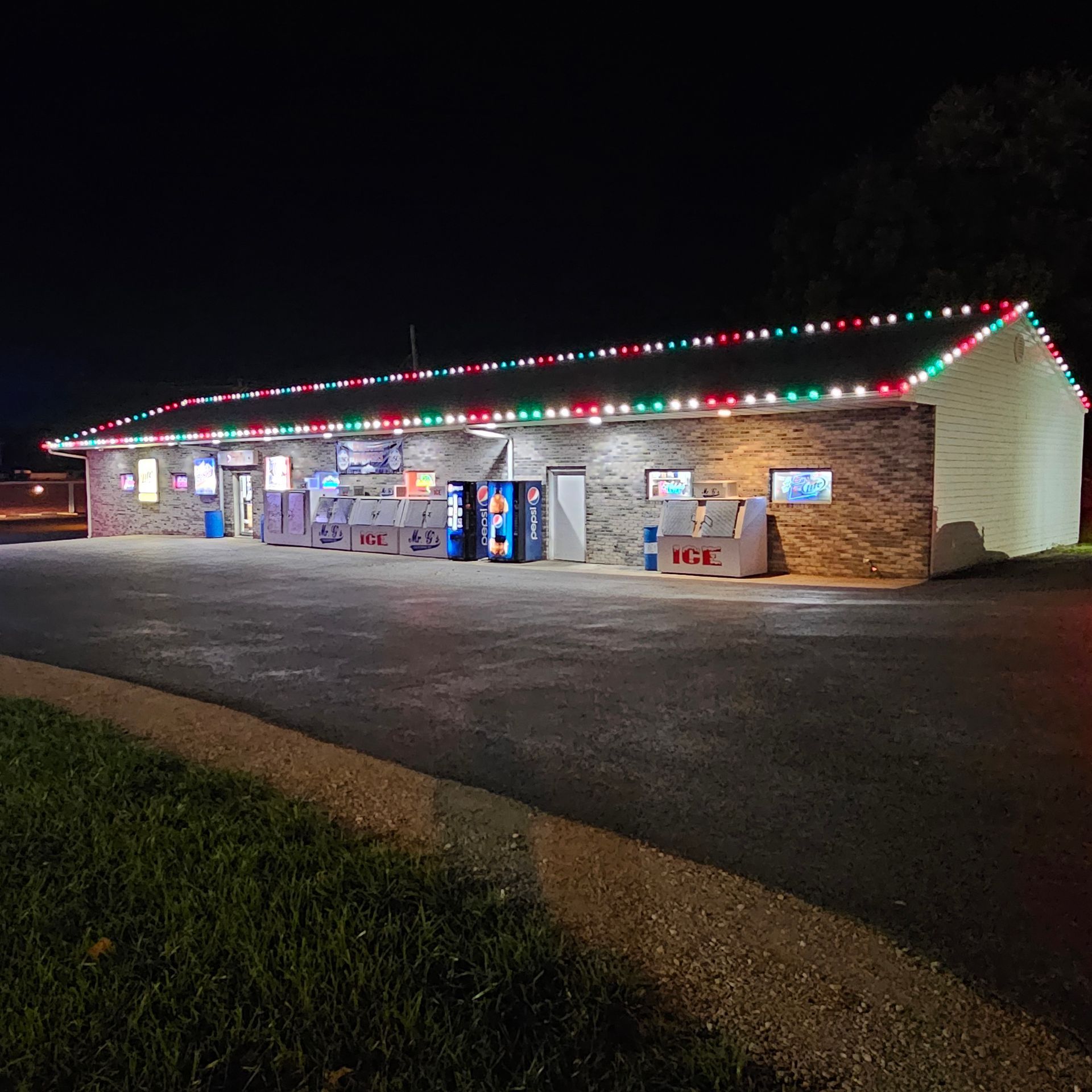 Nighttime storefront with bright holiday lights and a lit parking lot