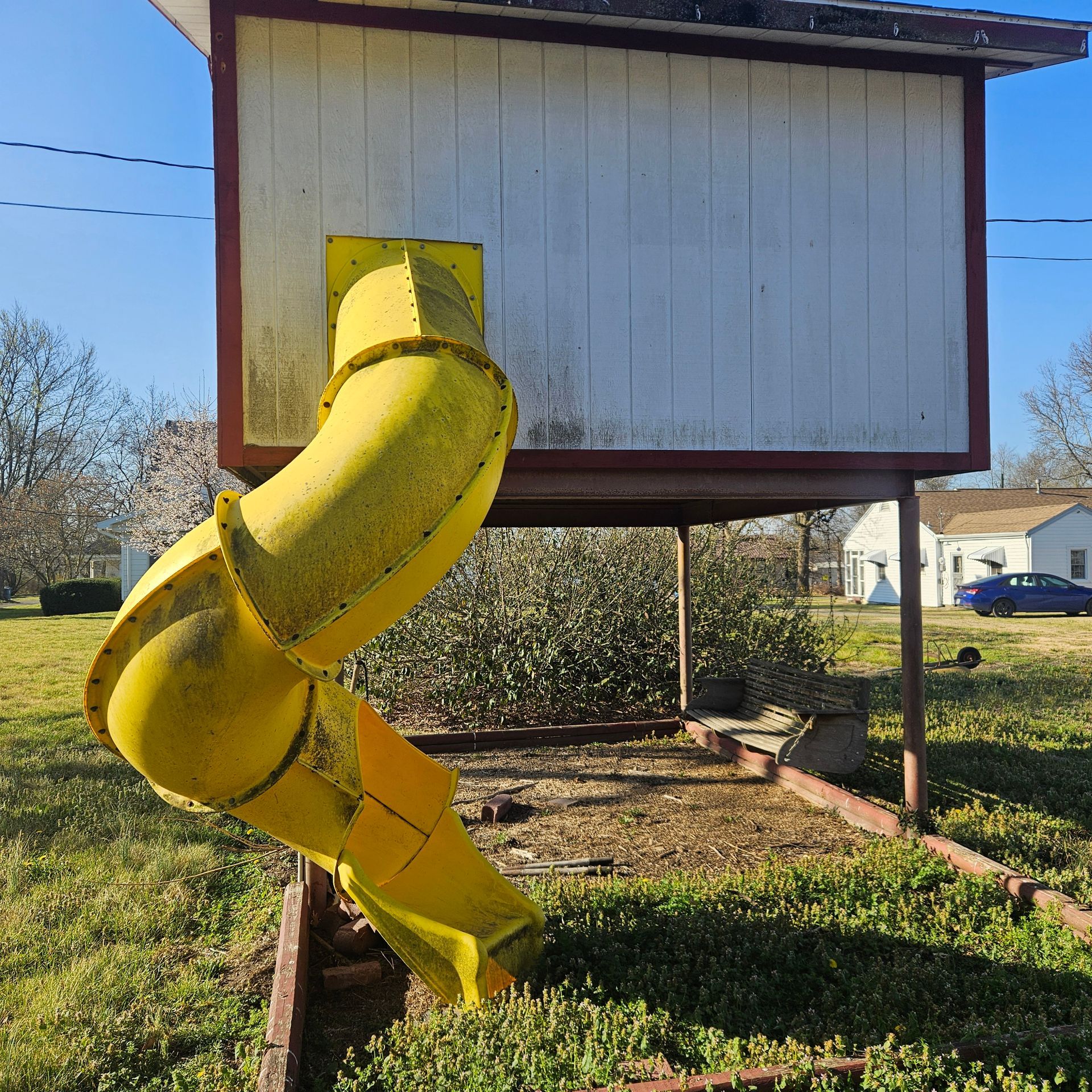 Yellow spiral slide attached to a small raised white playhouse in a grassy yard