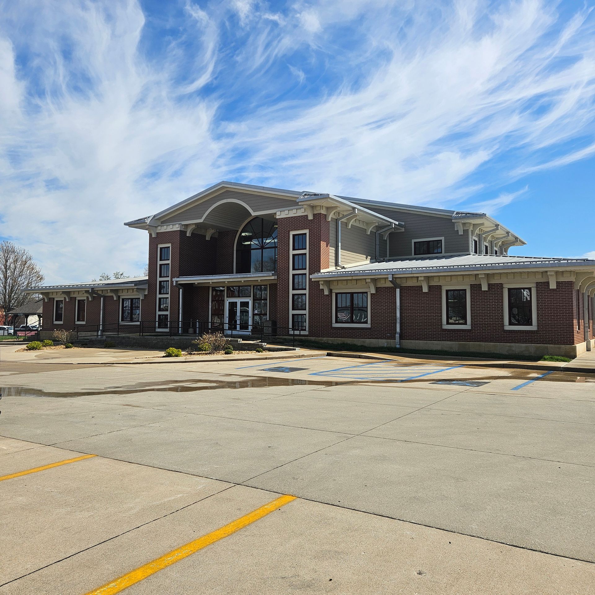 Large brick building with arched entrance, blue sky, and empty parking lot in front