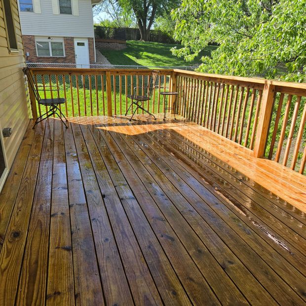 Wet wooden deck with railing overlooking a grassy backyard in bright sunlight