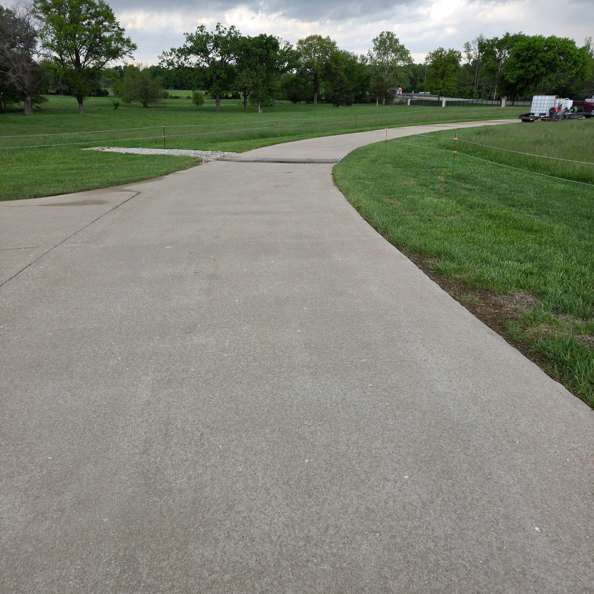 Curving concrete path through a green park with trees and open grass under an overcast sky