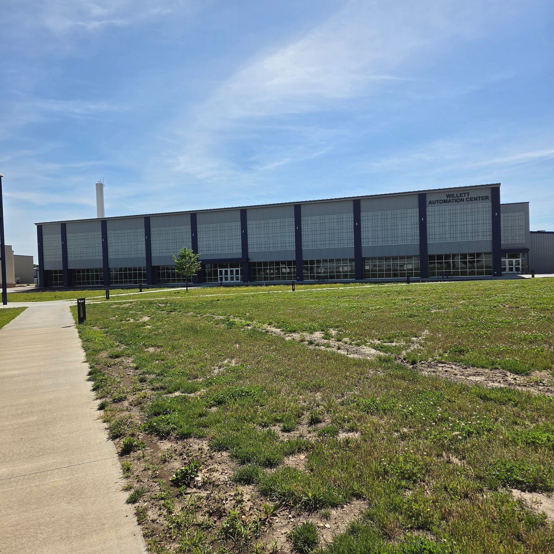 Modern low-rise building with a long facade beside a grassy field and sidewalk under a blue sky