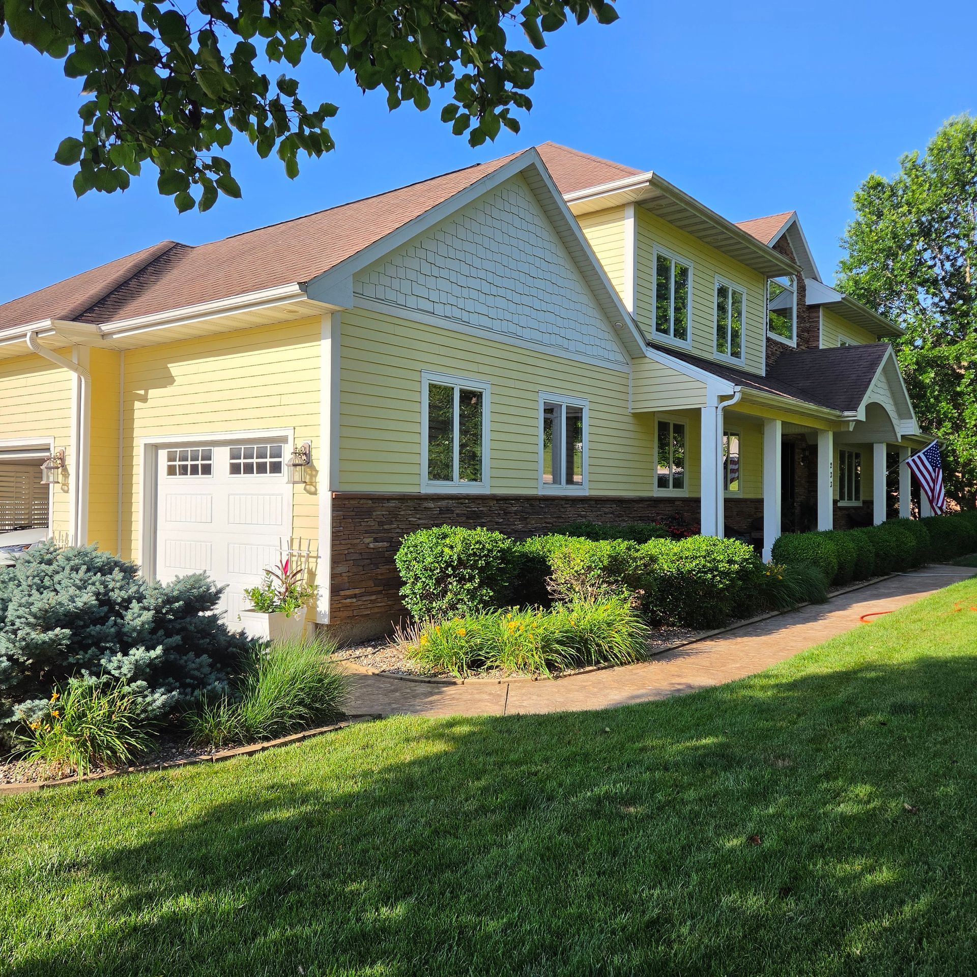 Yellow suburban house with white trim, garage, porch, and a green lawn under a clear blue sky