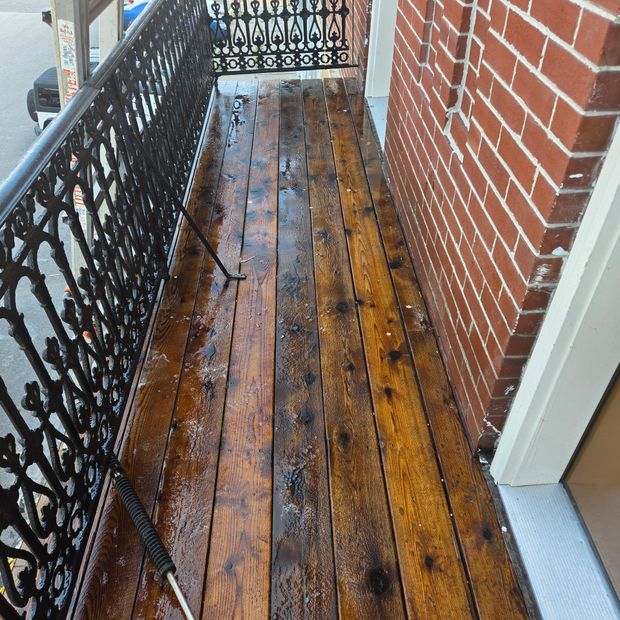 Narrow wet wooden balcony with black metal railing and brick wall beside it
